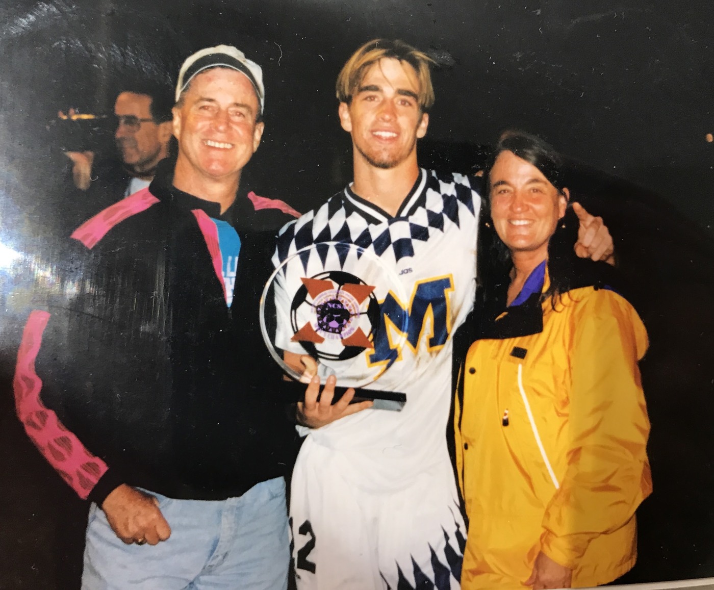 University of Michigan soccer player holding a trophy with his parents after a national final